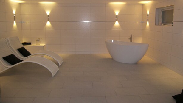 A modern bathroom with a freestanding bathtub, two wall-mounted lights, and two lounge chairs.