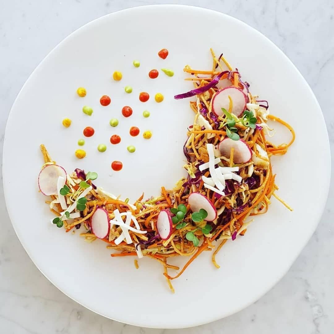 A white plate with a colorful salad, including shredded vegetables, radishes, and sprouts.