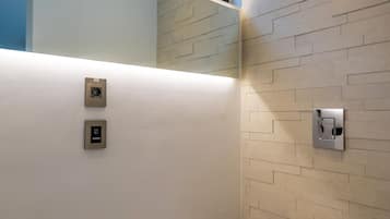 A modern bathroom with a toilet, a wall-mounted flush handle, and a window above the toilet.