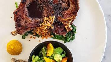 Un plato con un filete a la parrilla, guarnición de verduras mixtas y un recipiente pequeño con salsa.