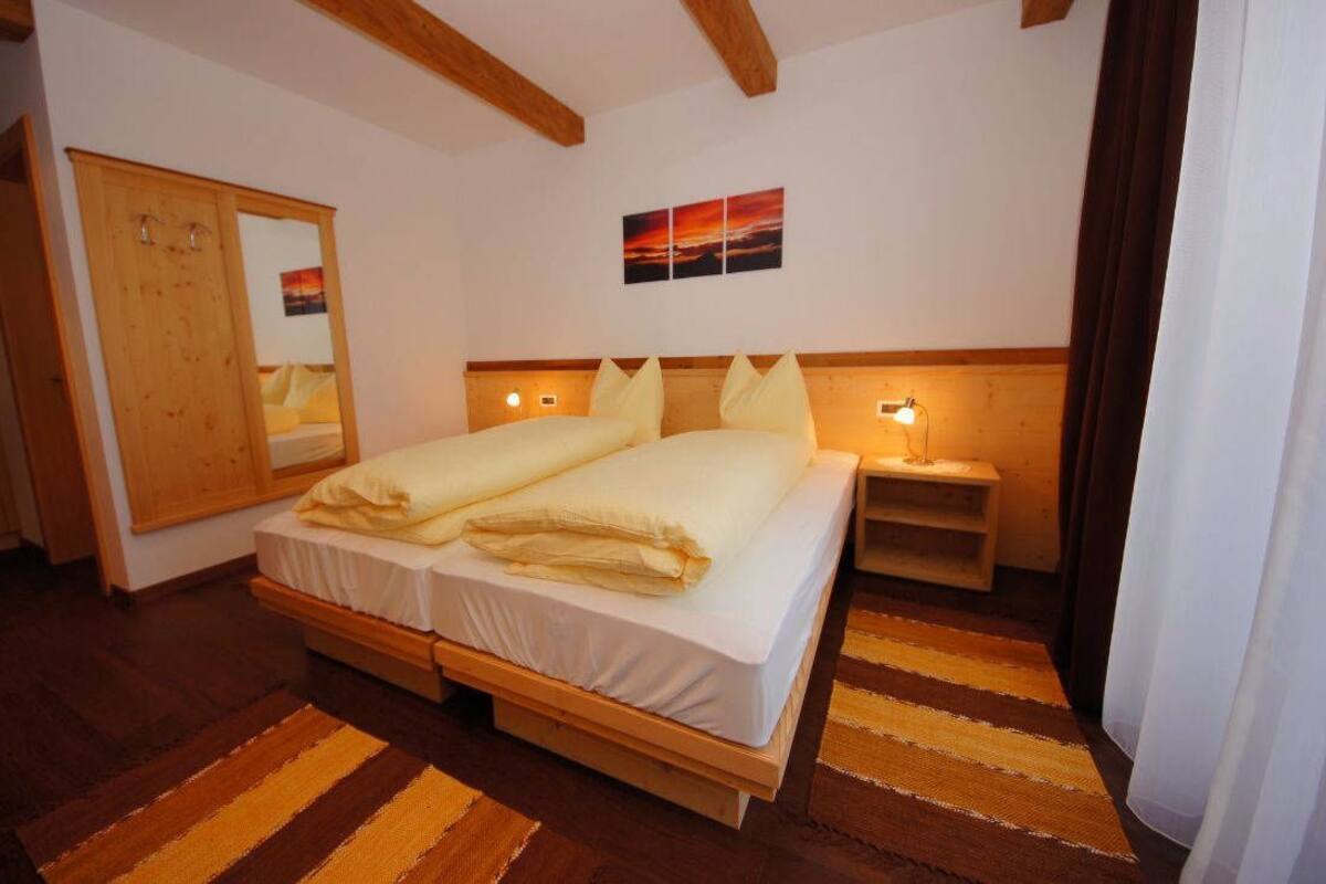 Ein Doppelbett mit Holz Kopfteil, ein Nachttisch mit Lampe, ein Holzkoffer und ein Streifen Teppich.