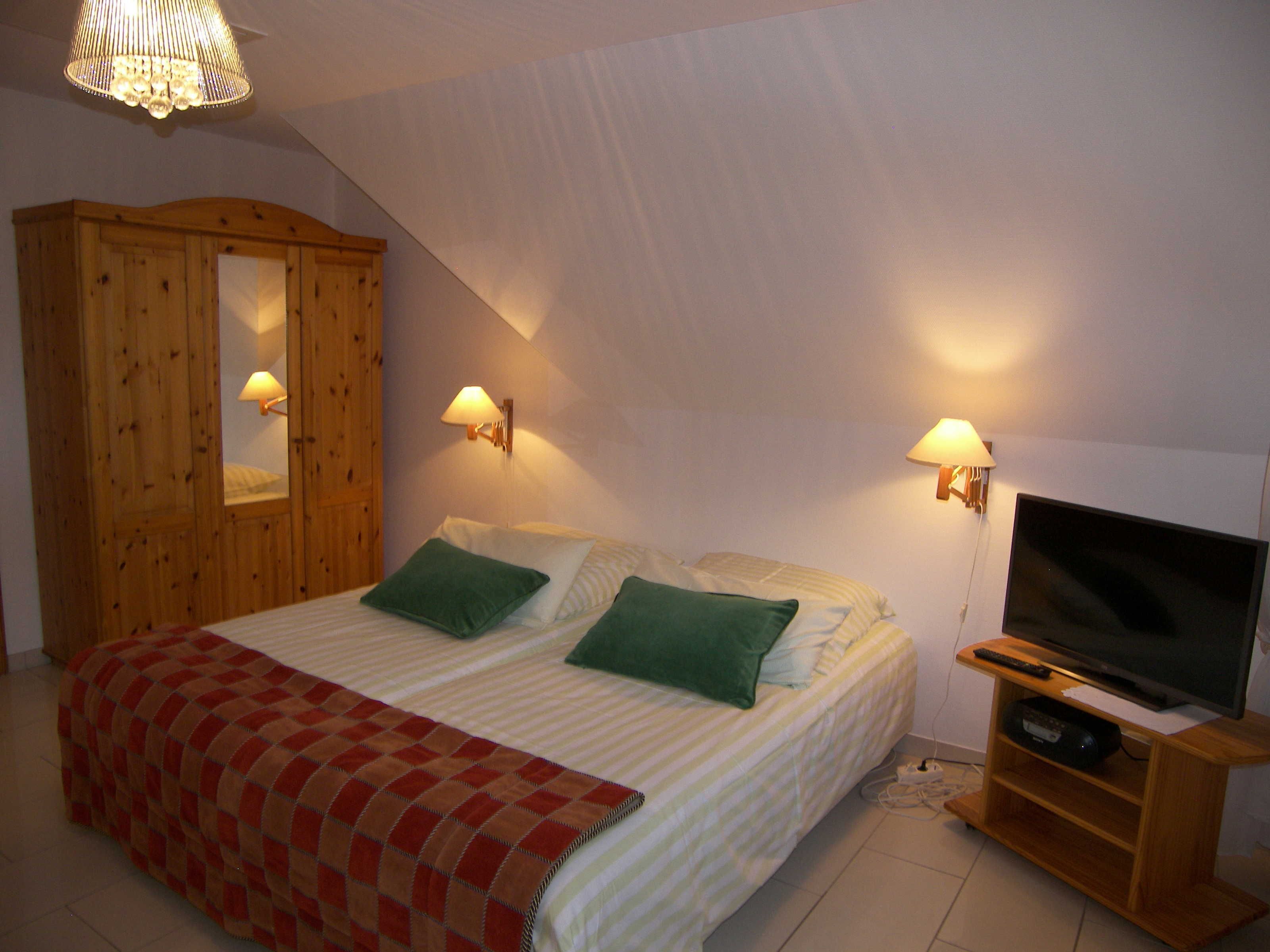 Un dormitorio con una cama, dos lámparas de noche, un mueble para televisión y un armario de madera.