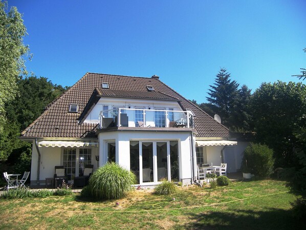 A two-story house with a balcony, a covered patio, and a lawn.