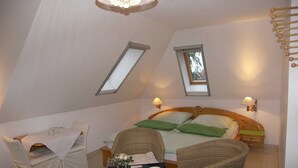 A bedroom with a sloped ceiling, two skylights, a bed with green pillows, a small table with a vase and bowls, and a wicker chair. - Vacation apartment 2 Seeadler - Holiday home 1A - 15 minutes by bike to the (Heringsdorf)