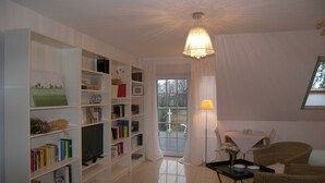 A living room with a bookshelf, a television, a dining table with chairs, and a window with curtains. - Vacation apartment 2 Seeadler - Holiday home 1A - 15 minutes by bike to the (Heringsdorf)