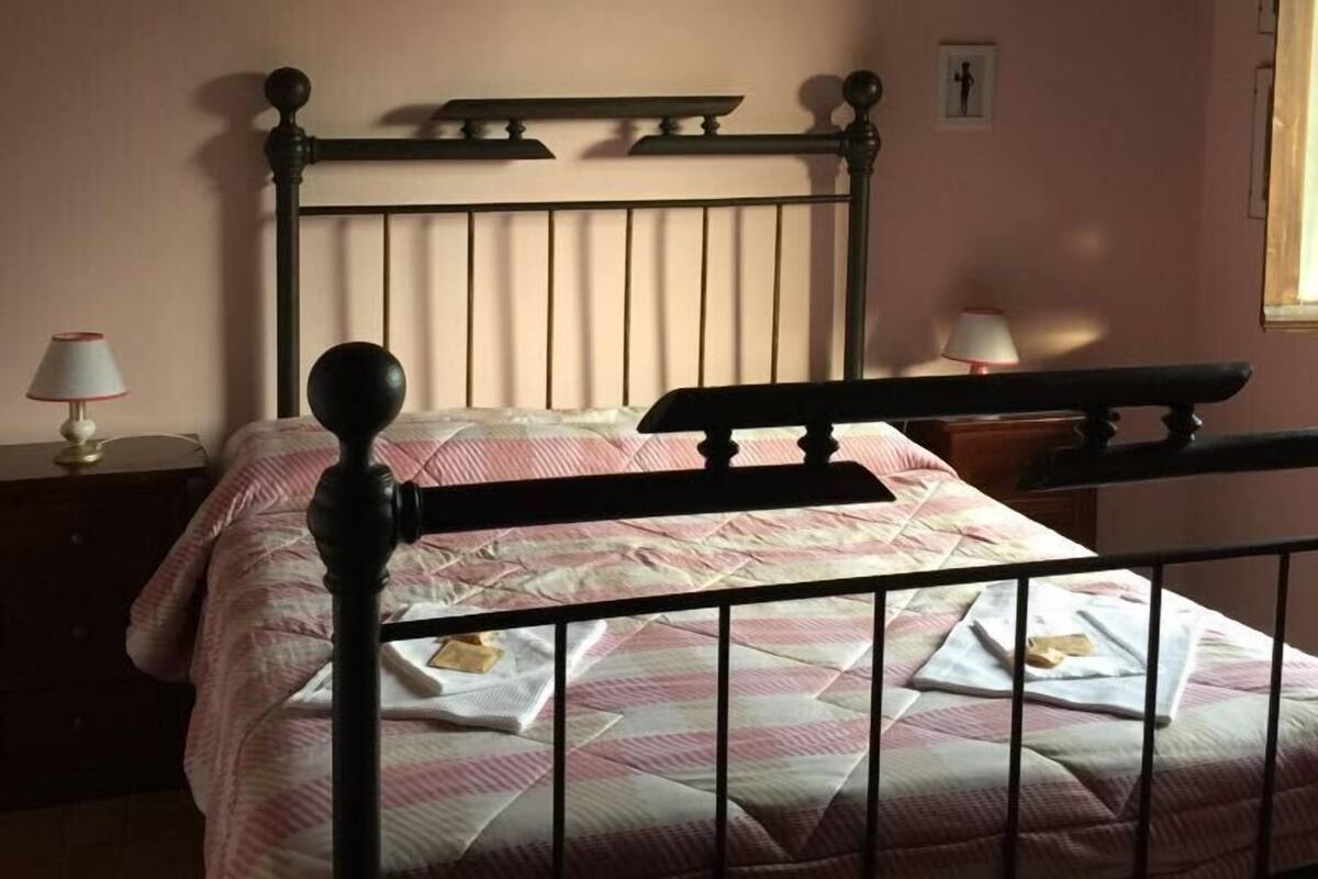Una cama individual con estructura metálica, una mesita de noche con lámpara, y un cuadro colgado en la pared.