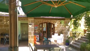 Een terras buiten met een tafel, stoelen, een groene parasol en stenen muren.