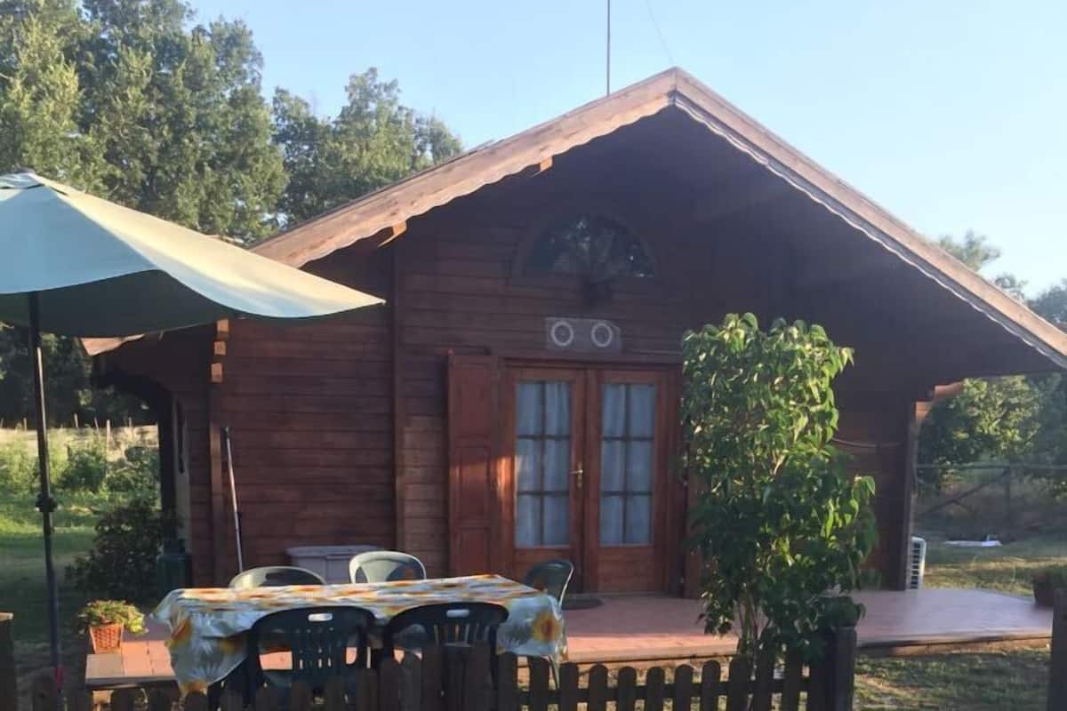 Una cabaña de madera con un porche, una mesa con sillas y un pequeño jardín.