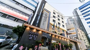 Et hotel med en moderne facade, et tydeligt skilt med 'SUGAR Seoul' og et 'HOTEL' skilt over indgangen.