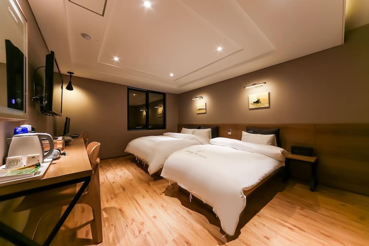 A hotel room with two beds, a desk with a chair, a flat-screen TV, and a mirror.