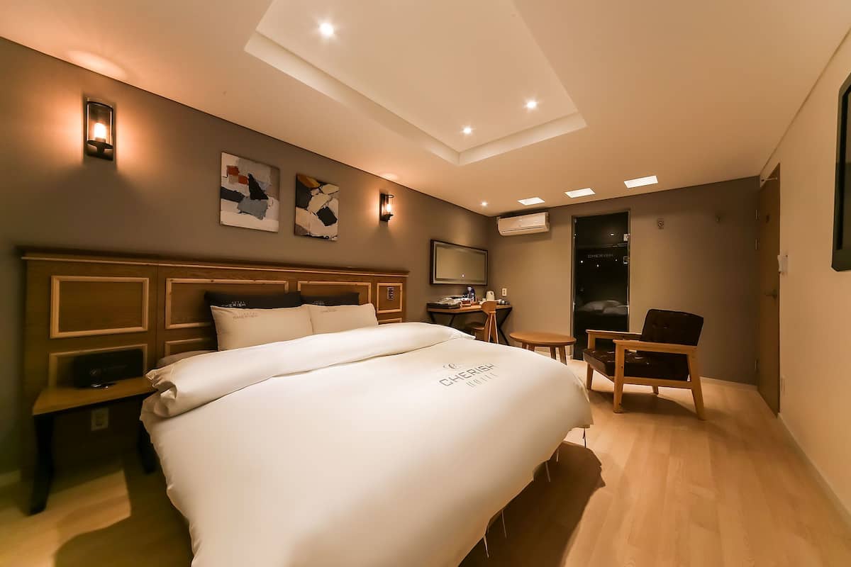 A hotel room with a large bed, a desk, a chair, and a TV.