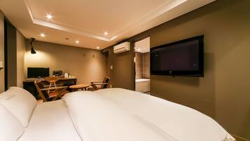 A modern hotel room with a large bed, a desk with a chair, a TV mounted on the wall, and an air conditioning unit.
