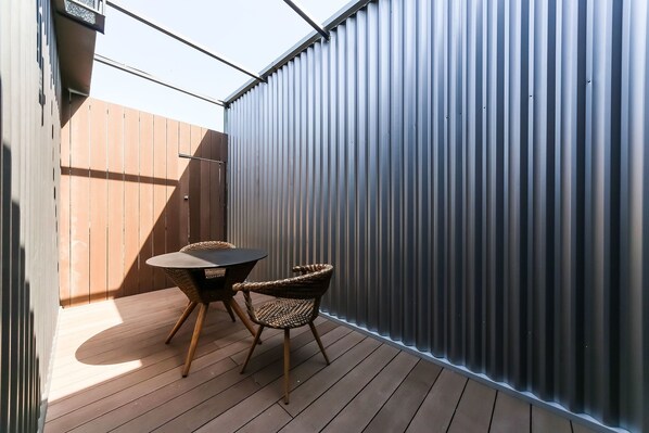 A small outdoor patio with a wooden deck, a round table, and two wicker chairs.