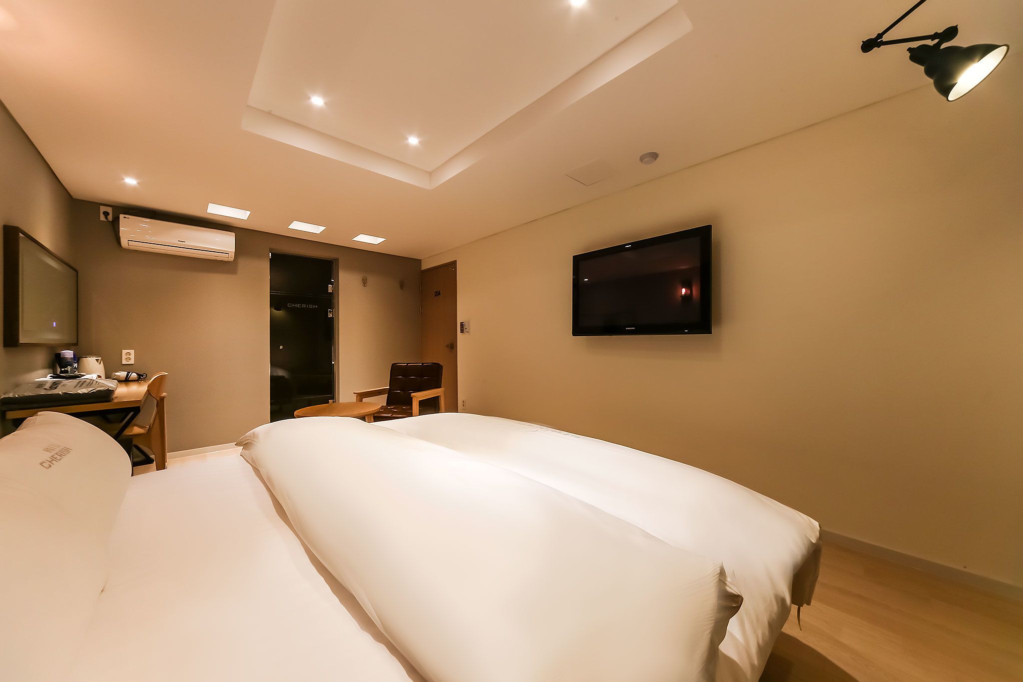 Una habitación de hotel con cama, escritorio, silla, televisor y aire acondicionado.