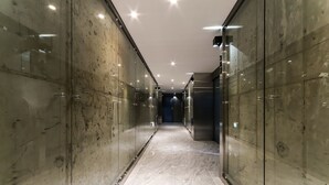 En moderne, veloplyst gang med marmorgulv og glasvægge, der fører til en elevator.