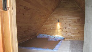 Ein kleines Dachzimmer mit Holzwänden, einem Bett, einer Wandleuchte und einer sichtbaren Tür.