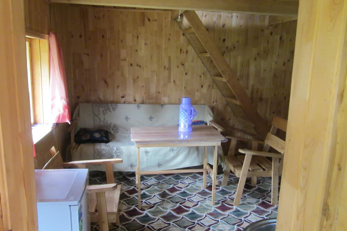 A wooden cabin with a patterned floor, a sofa, a table, and a chair.