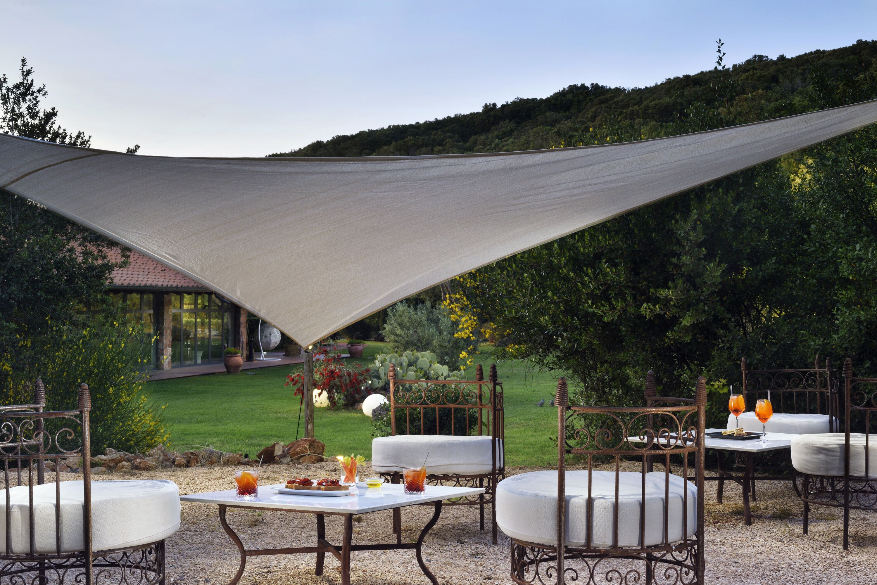 Patio esterno con tavolo e sedie, zona ombreggiata e vista giardino.