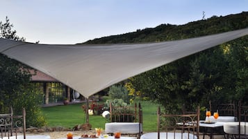 Patio esterno con tavolo e sedie, zona ombreggiata e vista giardino.