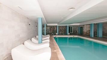 A swimming pool area with white lounge chairs and a stone wall.