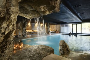 Une piscine agrémentée de formations rocheuses naturelles, dotée d’un éclairage chaleureux et offrant une vue sur l’extérieur grâce à de grandes fenêtres.