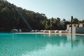 Une piscine à l’eau claire, entourée de chaises longues et bordée d’un bâtiment au design moderne.