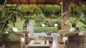 Una terrazza esterna con mobili in vimini, un tavolo con bevande e cibo, e vista su un giardino con cactus e alberi.