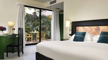 Habitación de hotel con una cama grande, un escritorio con lámpara y vistas a un jardín a través de una puerta corredera.