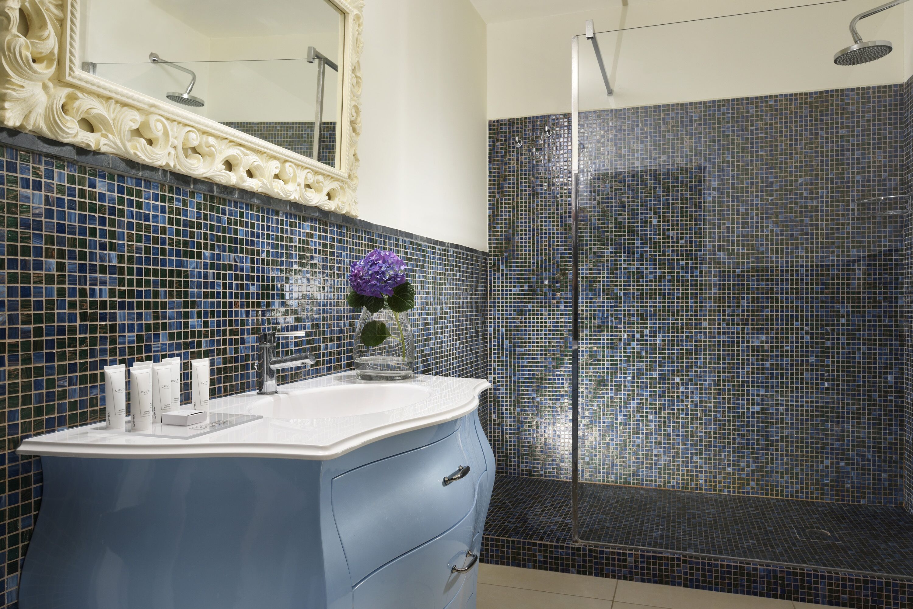 A bathroom with a blue vanity, a mirror, and a shower area.