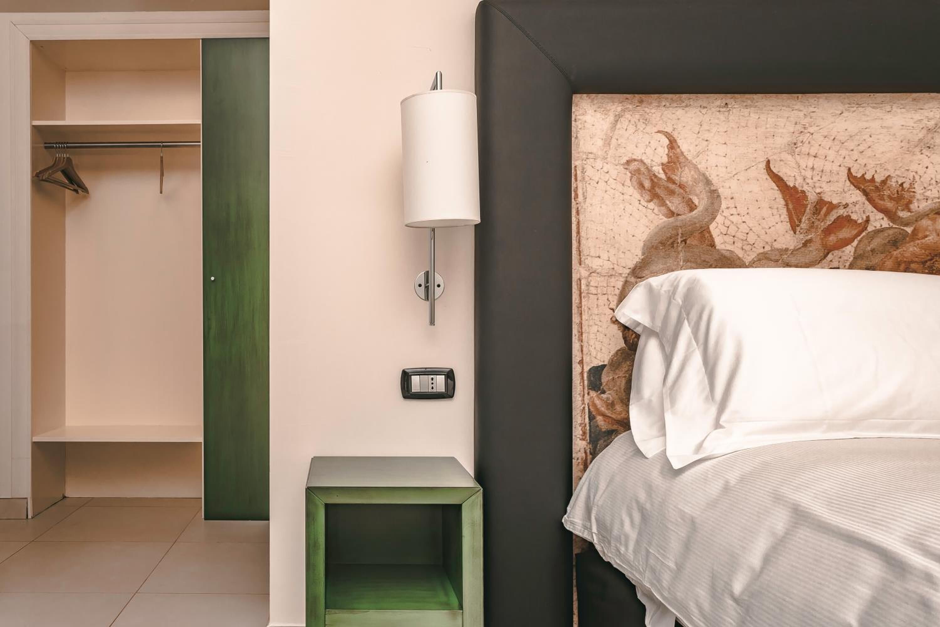A bedroom with a bed, a green nightstand, a wall-mounted lamp, and a closet with a green door.