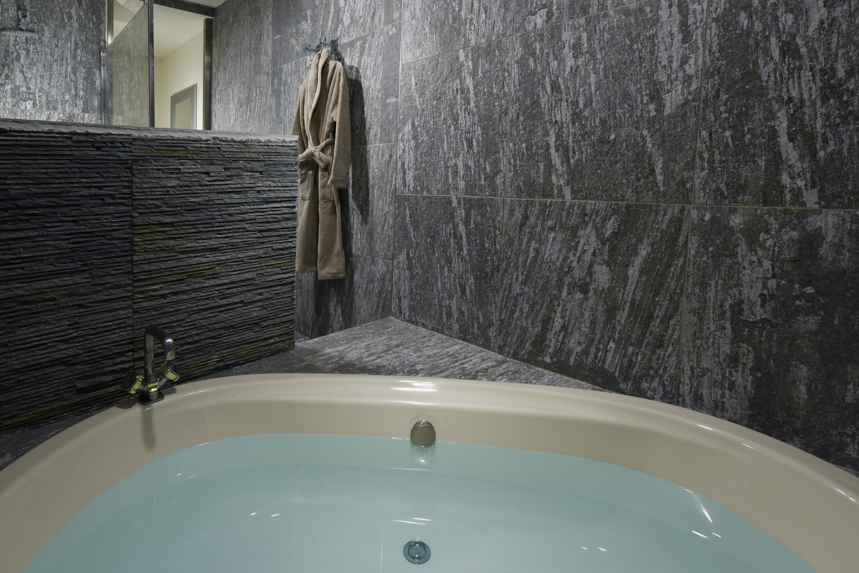 A bathroom with a bathtub, a towel rack, and a textured wall.