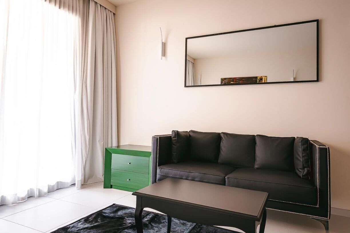Una sala moderna con un sofá de cuero negro, una mesita auxiliar verde, una mesa de centro negra y un espejo grande en la pared.