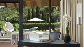 Un'area di lavoro esterna moderna con un laptop, un quaderno e un vaso con un'orchidea su un tavolo in vetro.