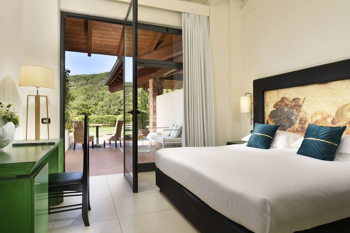 Een hotelkamer met een groot bed, een bureau, een stoel en uitzicht op een tuin en bergen.