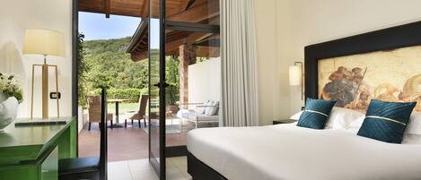 Habitación de hotel con una cama grande, un escritorio, una silla y vistas a un jardín y montañas.