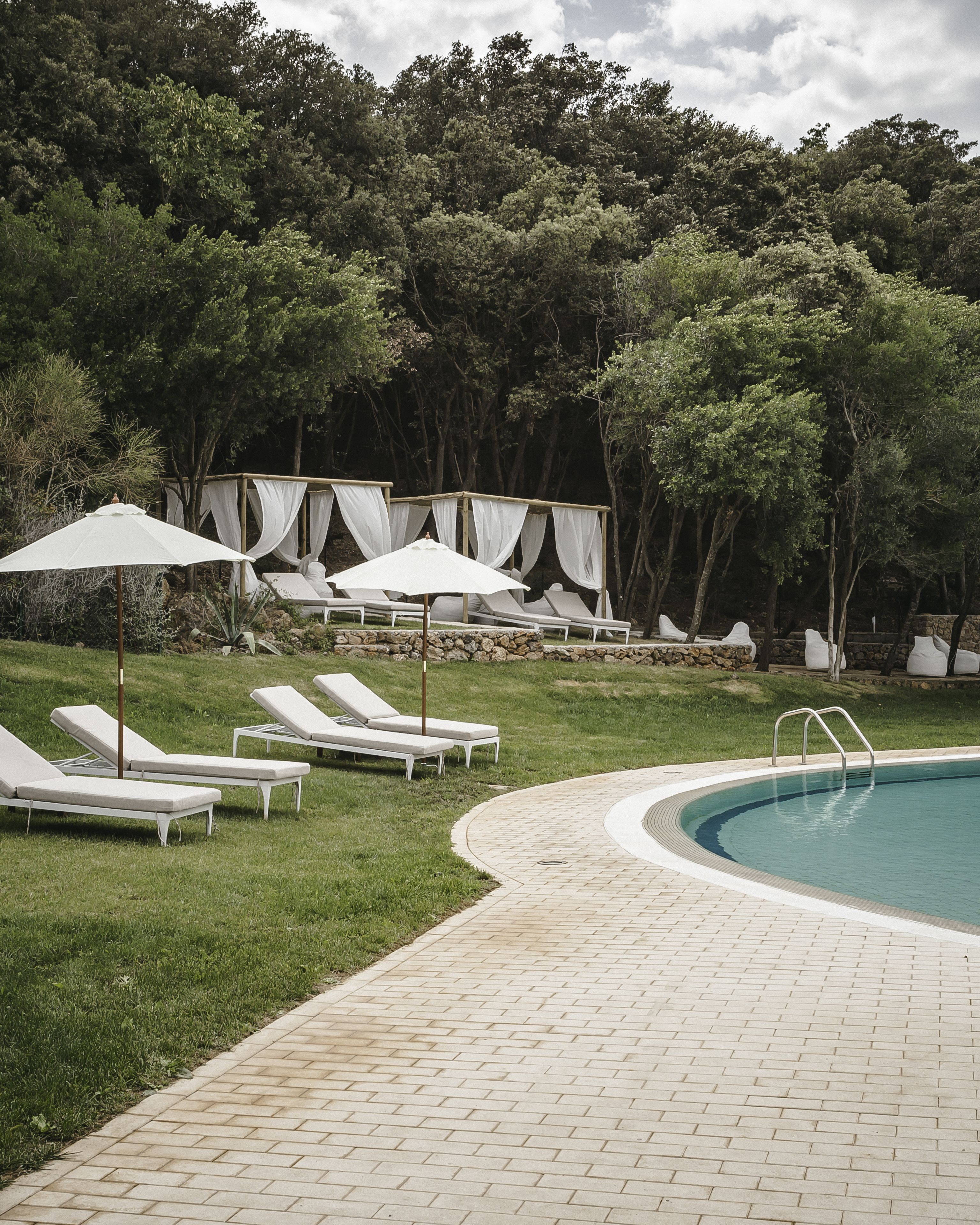 A poolside area with lounge chairs and umbrellas, surrounded by trees.
