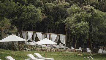 A poolside area with lounge chairs and umbrellas, surrounded by trees.
