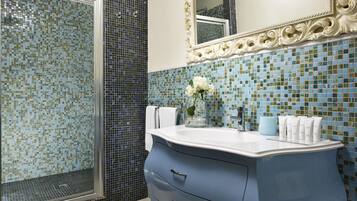 Un baño con ducha, un lavabo con artículos de aseo y un espejo con marco decorado.