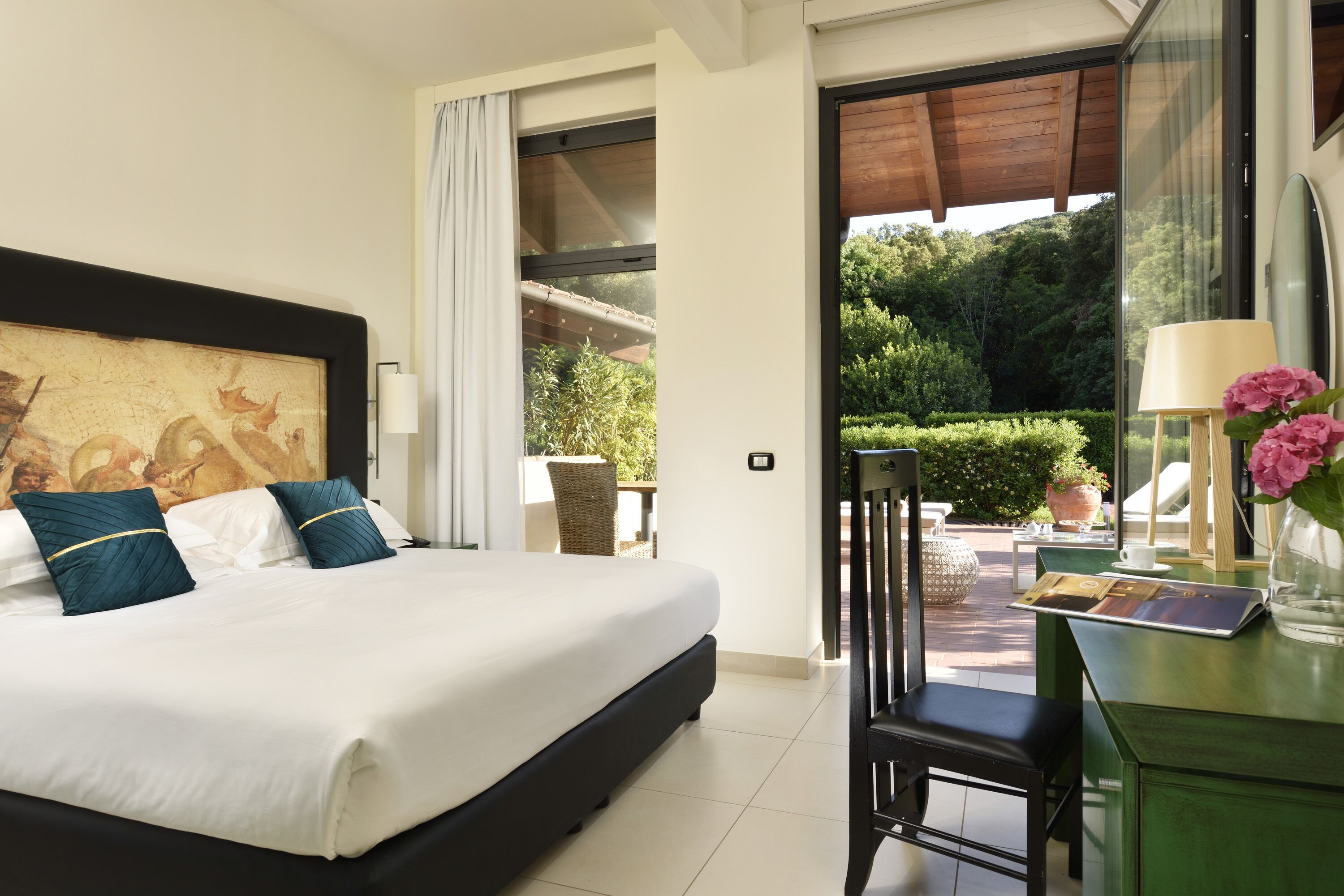 A hotel room with a large bed, a desk with a lamp, and a view of a garden.