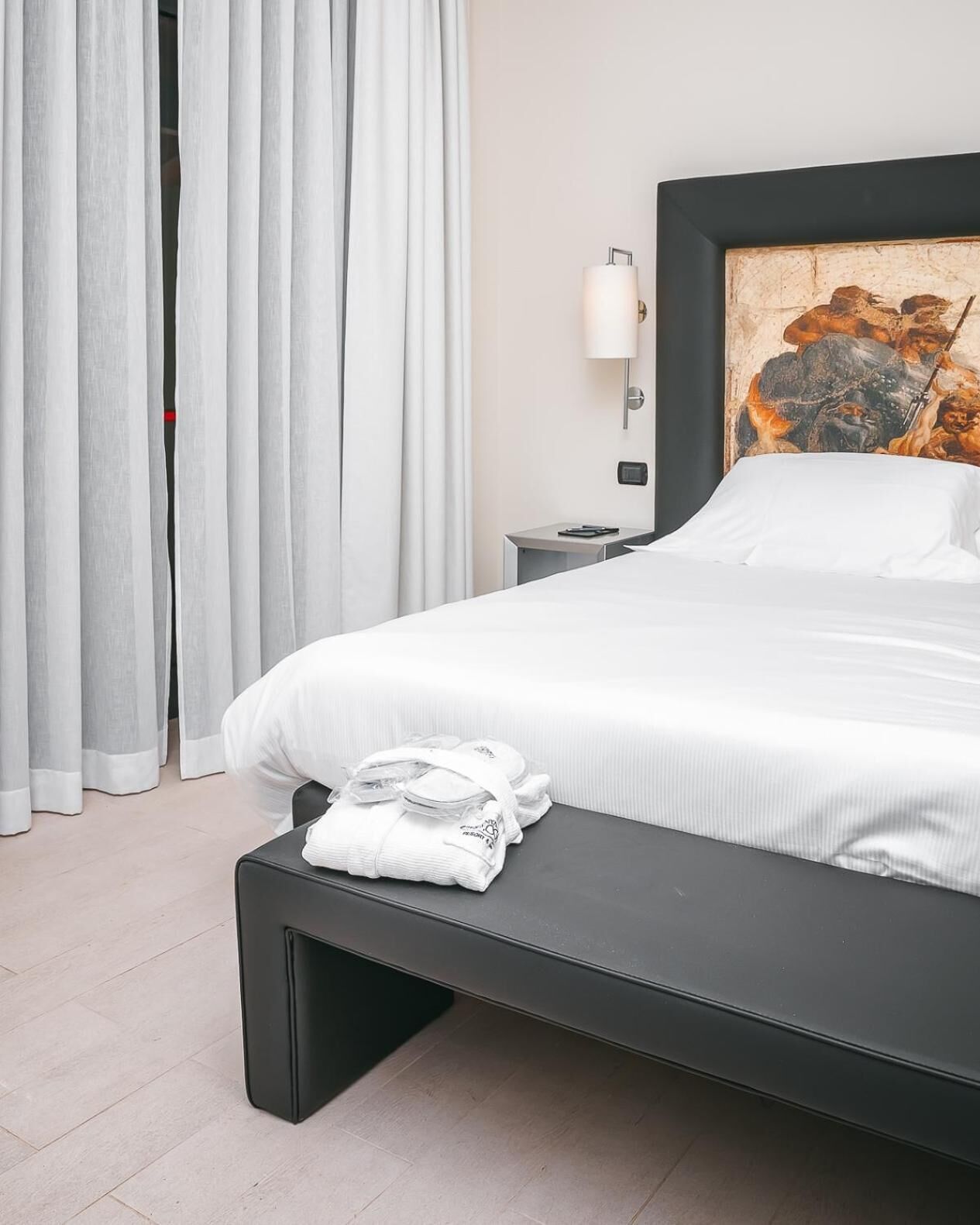 Habitación de hotel moderna con una cama grande, una mesita de noche, una lámpara y un cuadro en la pared.