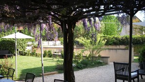 An outdoor patio area with tables and chairs, a pergola with purple flowers, and a garden in the background. - Maison de Marquay (Marquay)