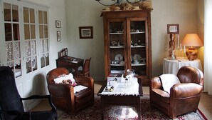 A traditional living room with leather armchairs, a wooden cabinet with glass doors, a chandelier, and a table with a lace tablecloth. - Maison de Marquay (Marquay)