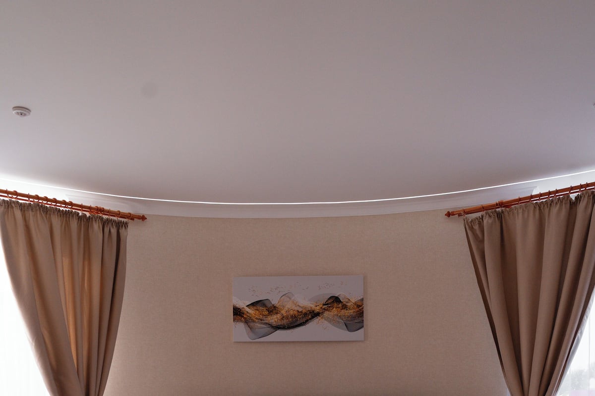 Quarto moderno com cama redonda, paredes bege e uma janela grande com cortinas.