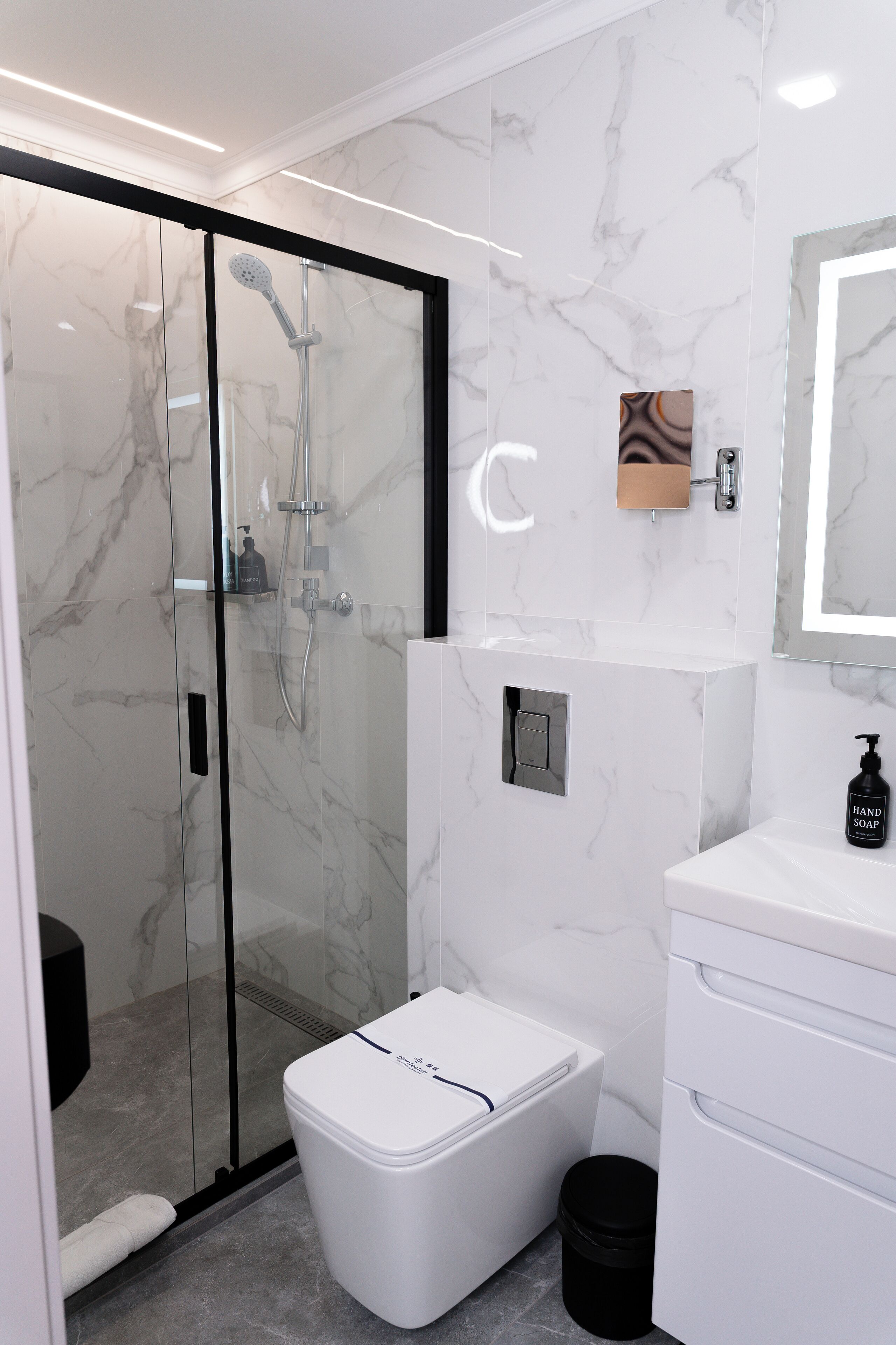 Une salle de bain moderne avec une douche à parois de verre, des toilettes blanches et un lavabo avec un miroir au-dessus.