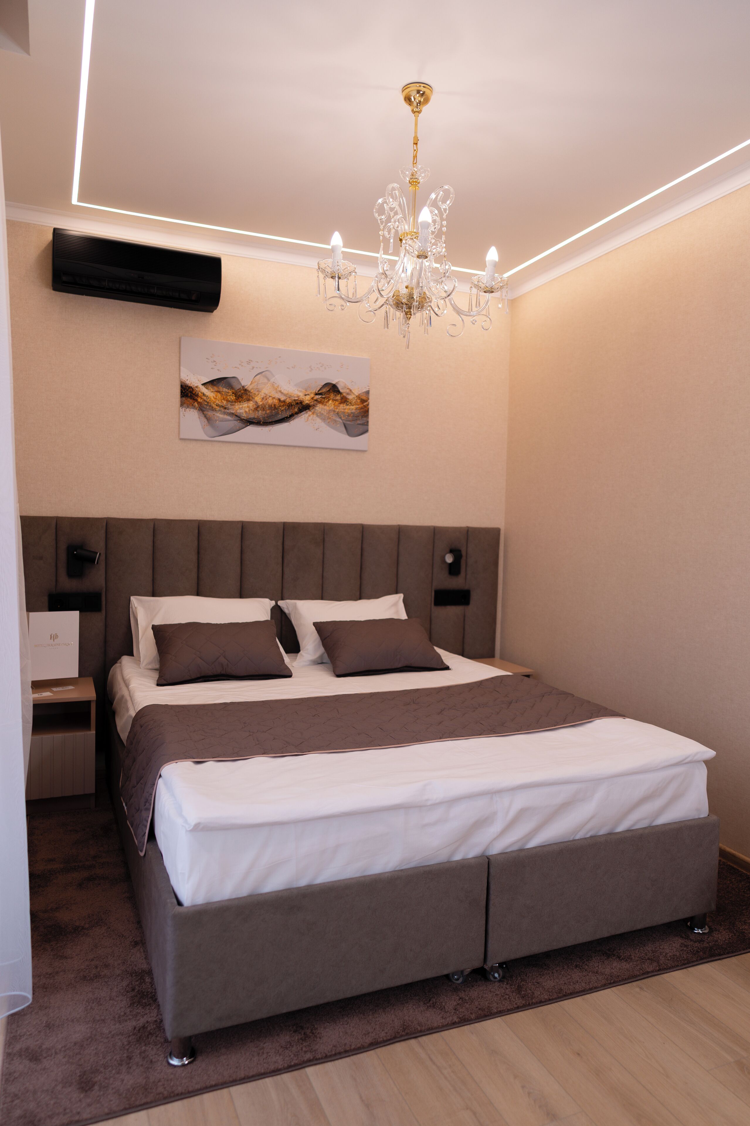 A modern bedroom with a large bed, a chandelier, and a wall-mounted air conditioner.