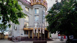Un hotel con un llamativo letrero 'UKRA', una entrada central con escalones y varias banderas.