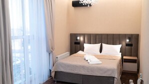 Habitación de hotel con una cama grande, una mesita de noche, cortinas translúcidas y un candelabro.