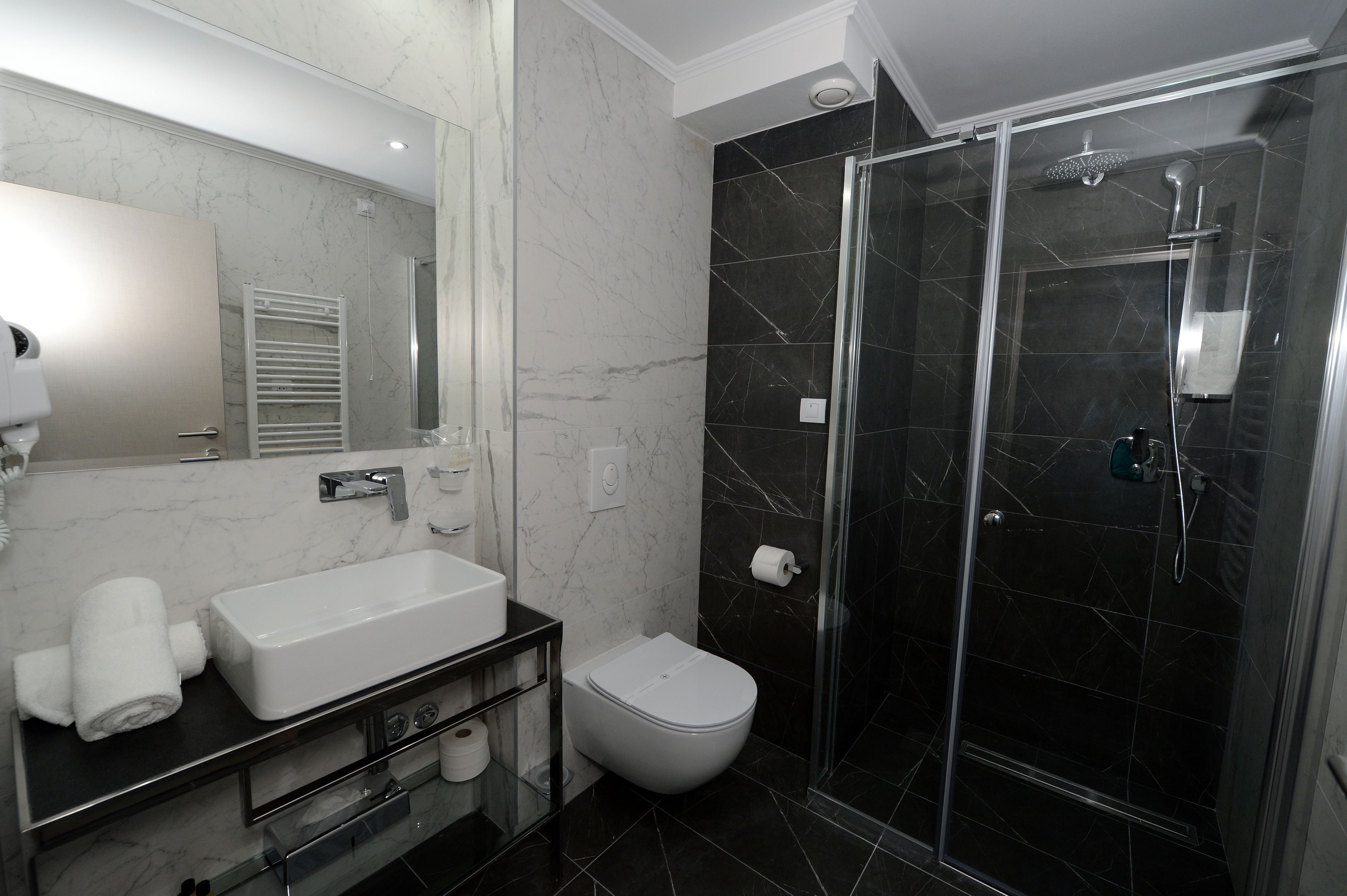 Un baño moderno con un espejo grande, un lavamanos blanco, un inodoro y una zona de ducha con mampara de vidrio.