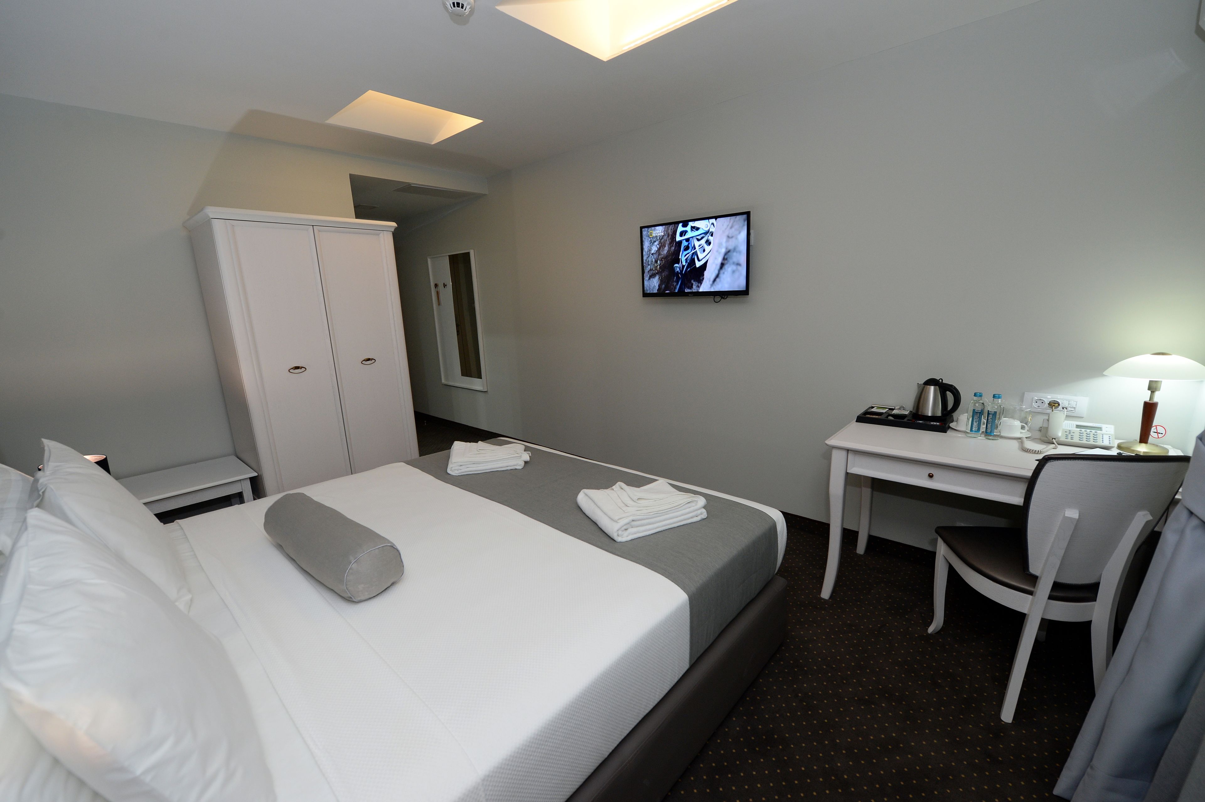 A hotel room with a bed, a desk, a chair, a TV, and a wardrobe.