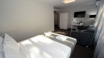 A hotel room with a bed, a sofa, a desk with a flat-screen TV, and a wardrobe.